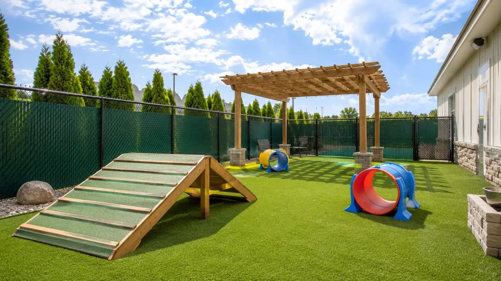 An outdoor dog play yard at a pet boarding facility with agility equipment